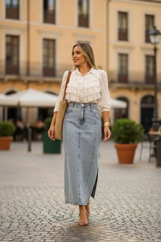Woman in a white blouse and denim skirt standing on a street with buildings in the background