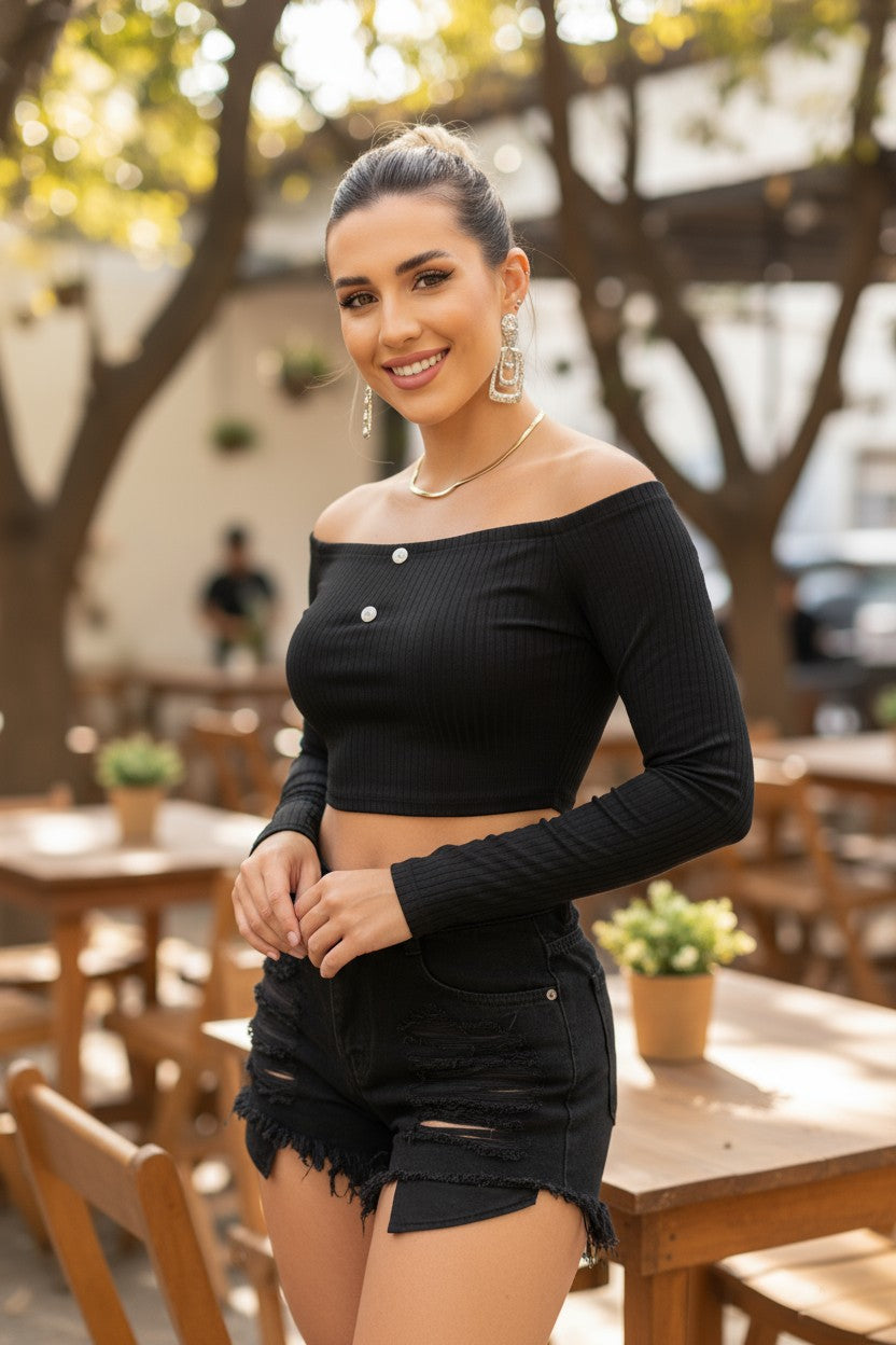 Woman in a black off-shoulder top and shorts standing outdoors with blurred background