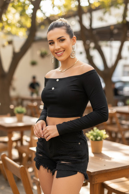 Woman in a black off-shoulder top and shorts standing outdoors with blurred background