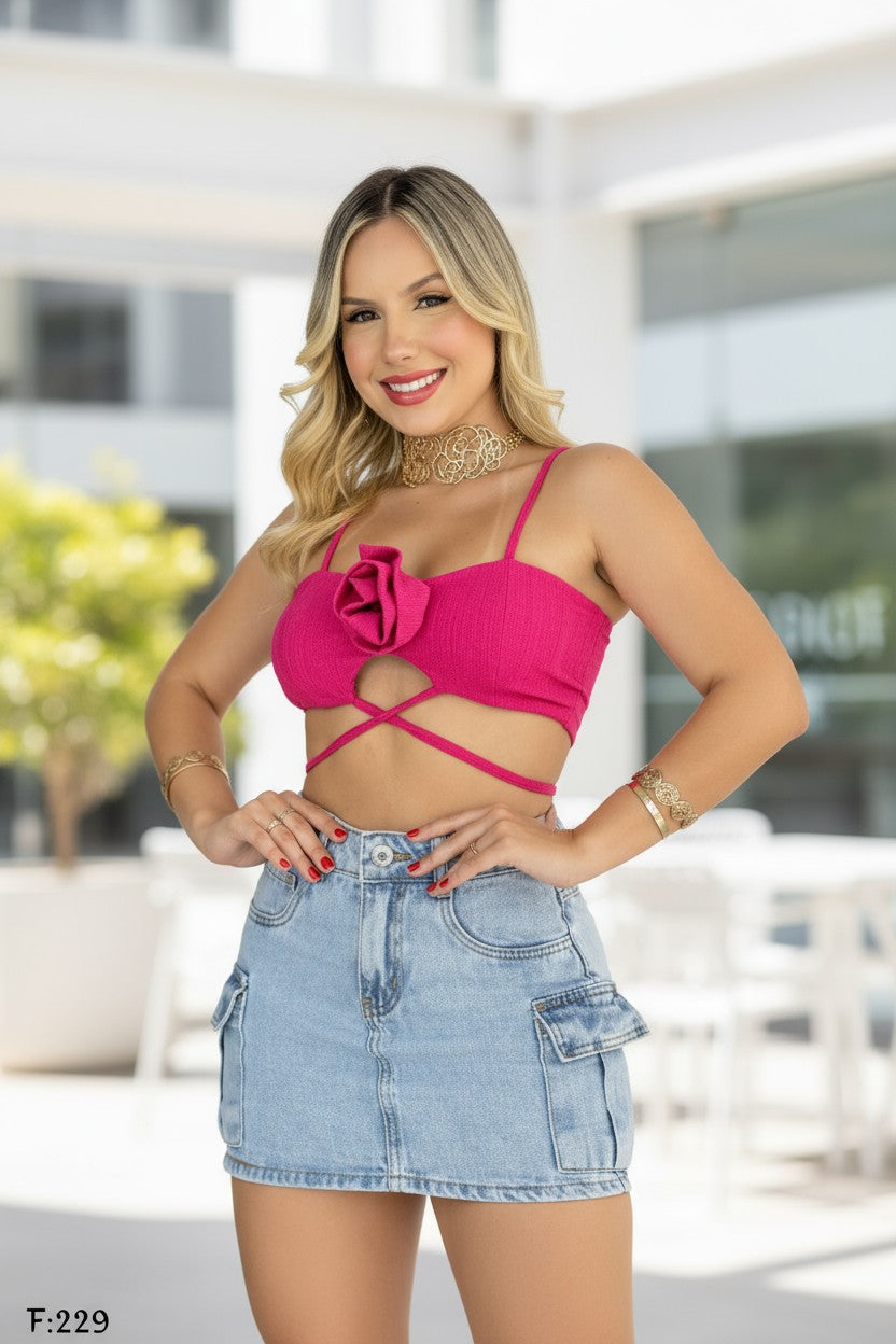 Woman wearing a pink top with floral design and denim skirt outdoors.