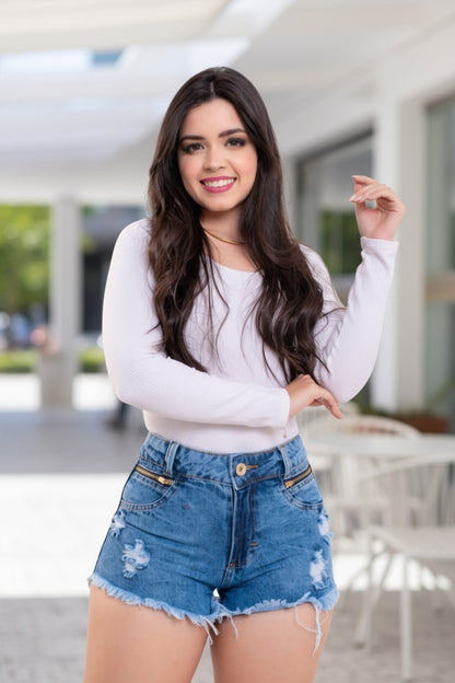 Woman wearing a white long-sleeve top and blue denim shorts outdoors.